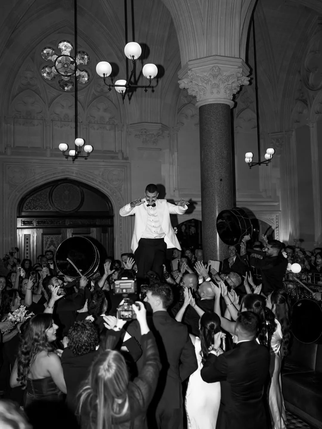 Groom lifted by the reception crowd in black and white